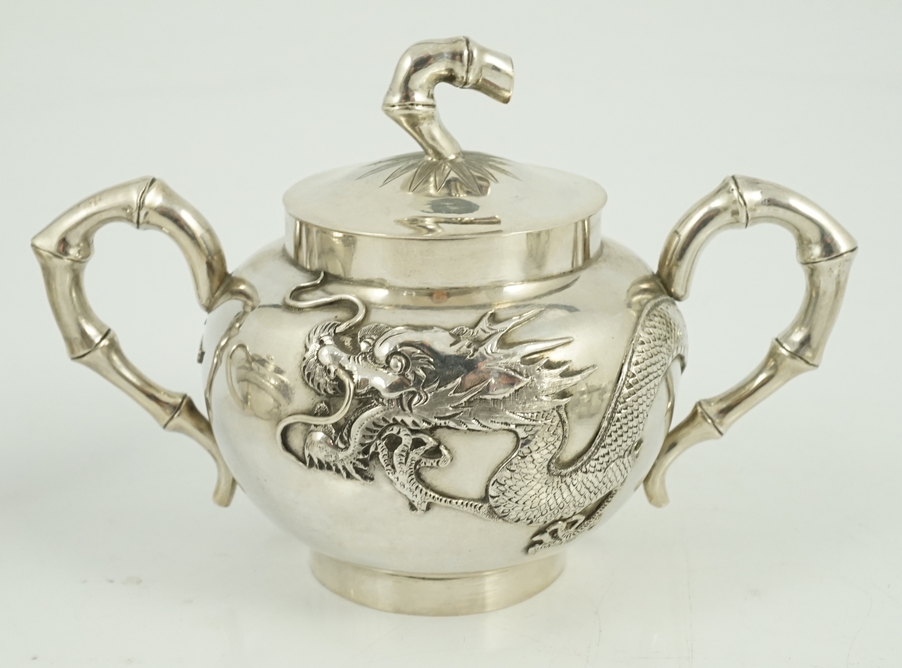 A Chinese three piece silver bachelor's tea set, by TC, decorated with dragon and one other similar Chinese silver two handled sugar bowl and cover, maker Sing Fat? and an odd cover